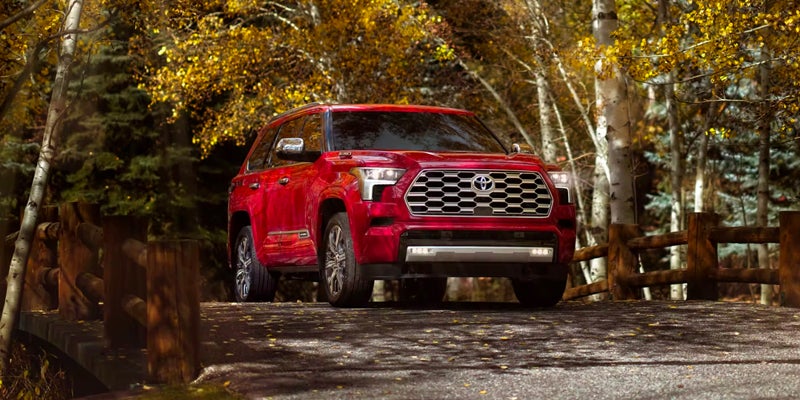 An all-new 2024 Radiant Red Toyota Sequoia driving across a little wooden bridge over a creek in the PNW. - Phil Meador Toyota Pocatello, ID