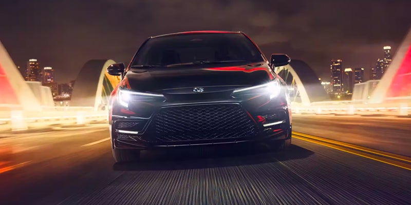 An all-new Black 2024 Toyota Corolla crossing a bridge leaving the downtown area and skyline in the background. - Phil Meador Toyota Pocatello, ID