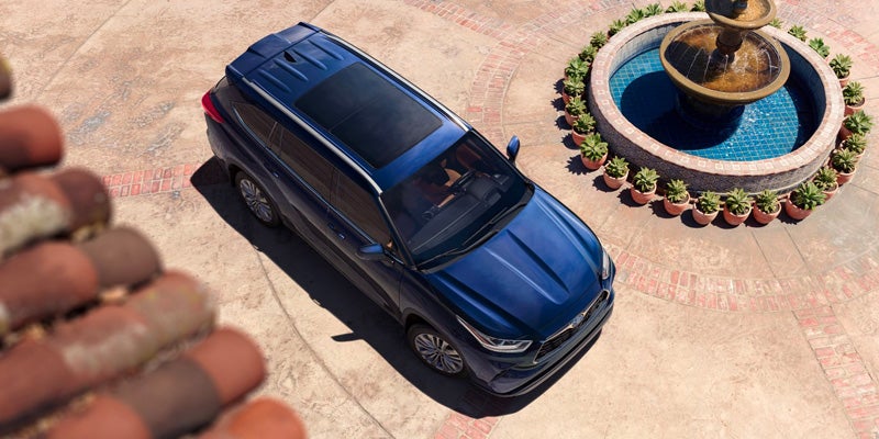 An all-new Blue 2025 Toyota Highlander Hybrid parked in a circular driveway next to a fountain. - Phil Meador Toyota Pocatello, ID