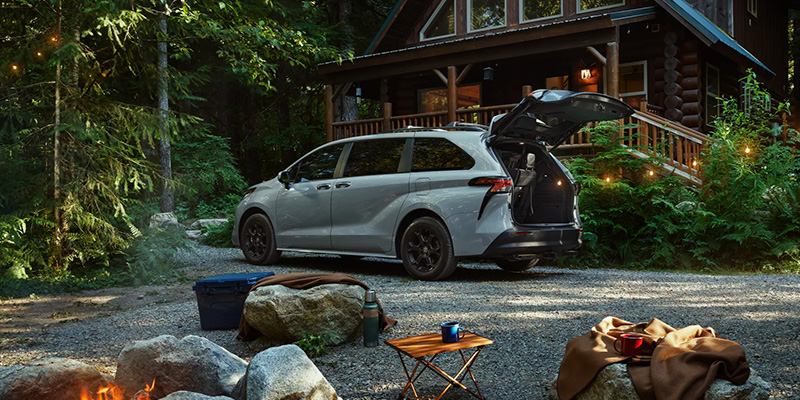 An all new grey 2025 Toyota Sienna parked outside a cabin in the woods with the trunk hatch ajar. - Phil Meador Toyota Pocatello, ID