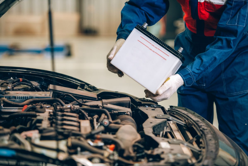 Mechanic replacing a car battery under the hood.